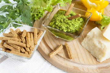Basil pesto with bread rusks parmigiano cheese fresh yellow pepper lettuce leaves parsley on wooden board and napkin background