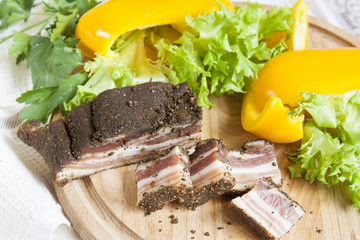 A delicious smoked ribs with spices around fresh yellow pepper lettuce leaves parsley on wooden board and napkin background