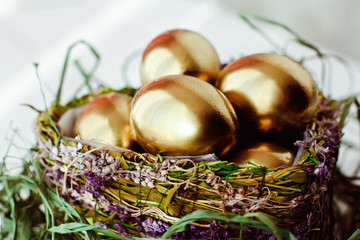 Golden easter eggs in nest on white wooden background