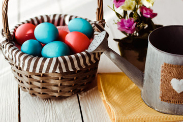Multicolored Easter eggs in wicker basket on white wooden background