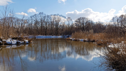 River in spring with snow-covered coasts and sky reflection