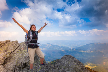 Obraz premium Young happy woman with backpack standing on top of the mountain.