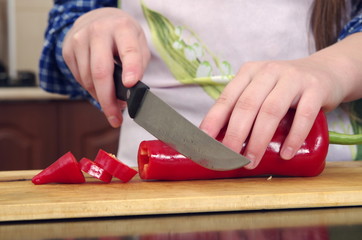 Little girl is cutting vegetables for salad closeup