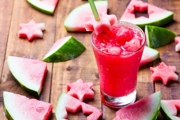 Glass of watermelon smoothie and pieces of watermelon on wooden background