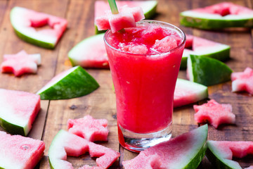 Glass of watermelon smoothie and pieces of watermelon on wooden background