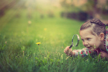 beautiful cute little girl with magnifying glass examining flower