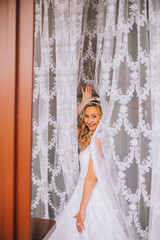 Beautiful blonde bride in wedding dress posing under curtain