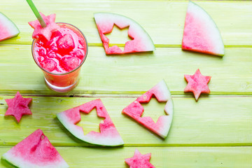 Glass of watermelon smoothie and pieces of watermelon on wooden background