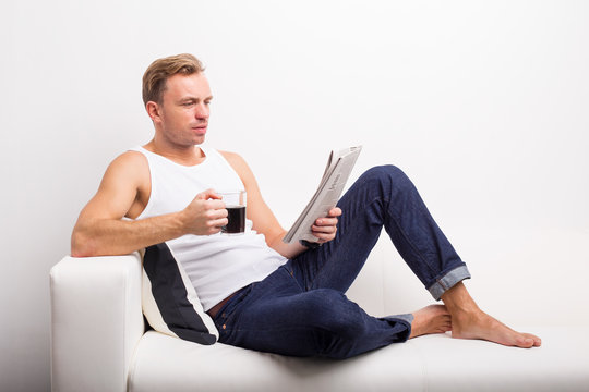 Man relaxing on couch with coffee mug and reading newspaper