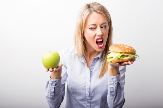 Woman choosing to eat burger instead of apple