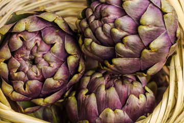 Obraz premium Fresh purple artichokes in wicker basket closeup background