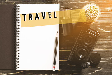 Notebook and pencil on rustic wood table with text ''TRAVEL''