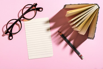 Paper sheet, glasses, notebook and pencil on pink paper board, t