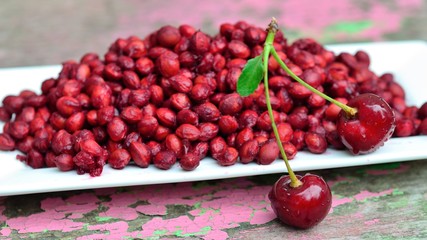 lot of cherry pits and two ripe cherries on a white dish on old wooden Board