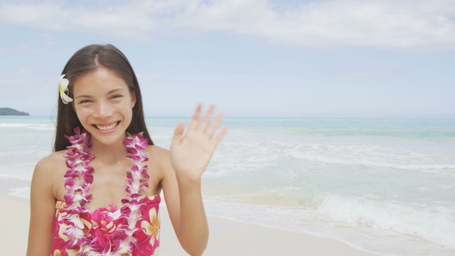 Happy beach woman waving hands hello saying on Hawaii showing Hawaiian aloha spirit wearing traditional flower lei garland. Portrait of multiracial Asian Caucasian woman on beach. RED EPIC SLOW MOTION