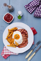 English breakfast with grilled ham, fried egg and french fries.
