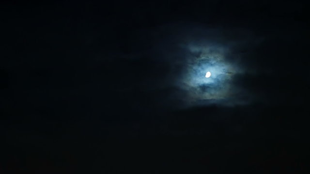 Storm clouds moving over the moon at night on overcast dark sky. Windy bad weather and horror scene. 4K UHD video footage.