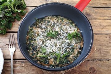 ortica, frittata con foglie di ortica in tegame di metallo sfondo rustico