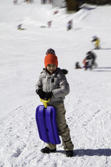 Fototapeta na wymiar child in the snow with blue toboggan