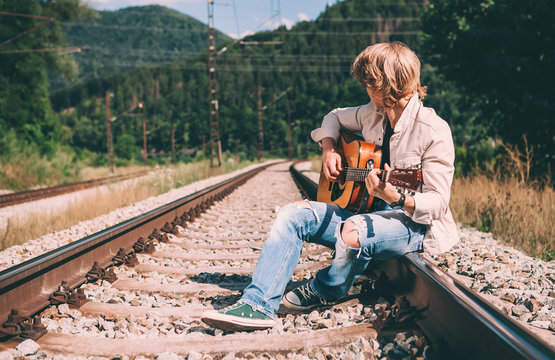 Young man with guitar sitting on the railway