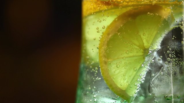 Color footage of a slice of lemon in a glass of soda, with ice cubes.