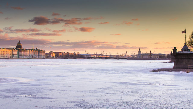Russia, Saint-Petersburg, 19 March 2016: The water area of ​​the Neva River at sunset, the Winter Palace, Palace Bridge, the dome of St. Isaac's Cathedral, pink clouds, frozen river