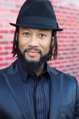 Vertical image of stylish African man wearing a suit and a hat on a bright and modern red background
