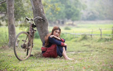 Pretty asian girl sit next to tree and bicycle in field