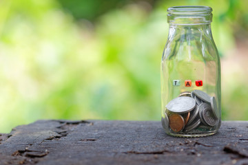 A jar filled with coins on old wooden table. With TAX word on the jar. Tax concepts.