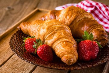 Fresh croissants with strawberries on plate, breakfast food, warm tone