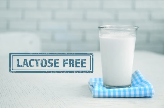 Glass of milk on wooden table and lactose free sign, on bricks wall background