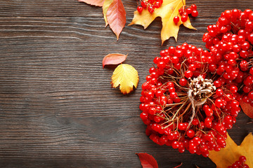 Autumn composition: bunch of viburnum and colourful leaves on wooden table