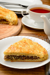 Piece of pie with minced meat on wooden table.