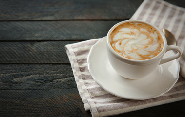 Cup of hot cappuccino with froth and spoon on a black wooden table