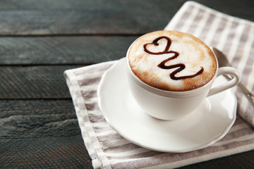 Cup of hot cappuccino with chocolate syrup and spoon on a black wooden table
