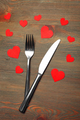 Fork and knife with decorative paper hearts, on wooden background