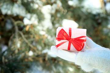 Woman hand in knitted mitten holding gift on winter background