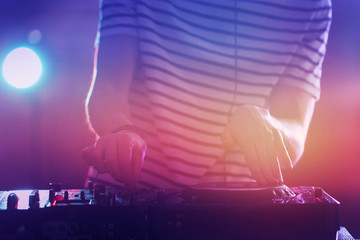 DJ playing music at mixer on colorful blurred background
