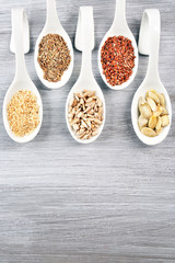 Different kinds of seeds in spoons on wooden table