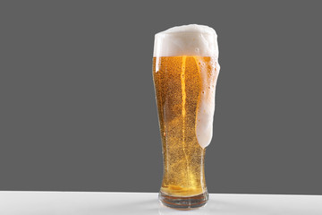 Glass of lager beer with thick froth on grey background