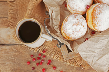 Delicious sugary donuts with red currant on wooden tray with parchment closeup