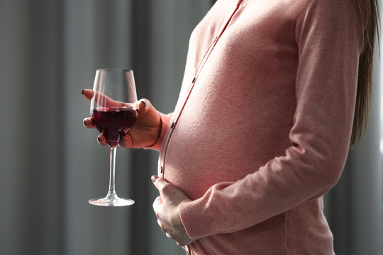 Pregnant woman with glass of red wine in hand indoors