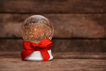 Christmas snow globe with red ribbon bow on wooden background