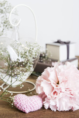 Carnation flowers and pink knit heart on wooden table