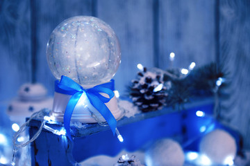 Christmas snow globe with blue bow in snow on wooden background