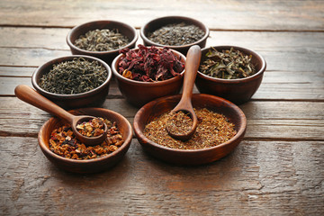 Variety of tea in round bowls with spoon on wooden table, close up