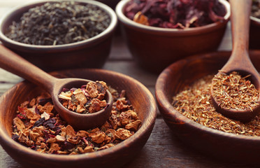 Variety of tea in clay bowls with spoon on wooden table, close up