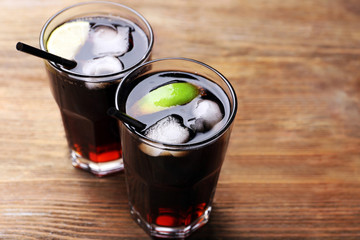 Cocktails with lime slices and ice blocks on wooden table, close up