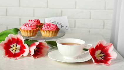 Fresh tulips with cupcakes and cup of tea on brick wall background