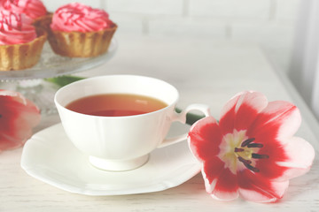 Fototapeta na wymiar Fresh tulips with cupcakes and cup of tea on wooden table closeup